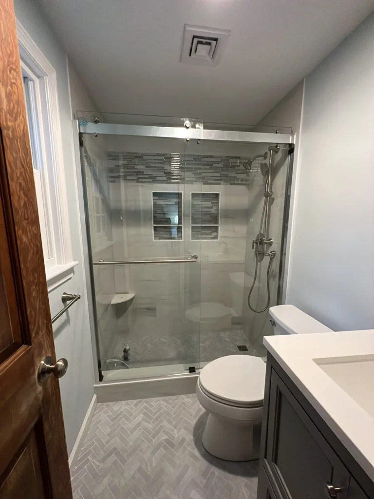 renovated bathroom with walk-in glass shower, gray tile, double recessed niches, handheld shower fixture and gray vanity