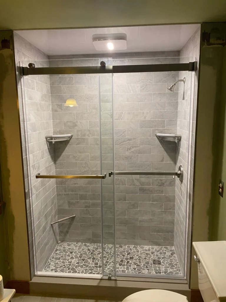 renovated bathroom with walk-in shower, sliding glass doors, gray wall tile and stone mosaic shower floor