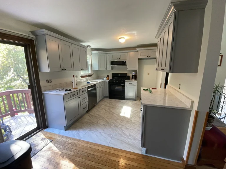 renovated kitchen with gray shaker cabinets, white quartz countertops, light tile flooring, black appliances and peninsula cabinetry